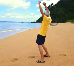 Japanese castaway at Sotobarani Island raising his arms looking at the ocean